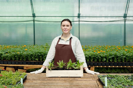 Confident female farmer in workwear standing by workplace inside large hothouse