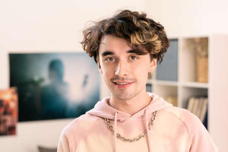 Contemporary teenager in pink hoodie looking at camera in home environmentの写真素材