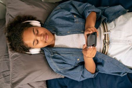 View of teenage girl listening to music in headphones while relaxing on bedの写真素材