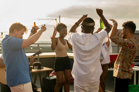 group of young ecstatic intercultural friends dancing at rooftop party