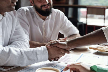 Two Muslim businessmen shaking hands over financial papers on workplaceの写真素材