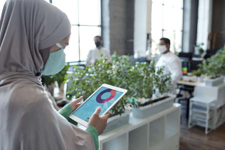 Young businesswoman in hijab looking through online data on tablet display
