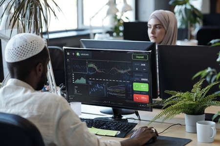 African Muslim businessman sitting in front of computer monitor in working environment