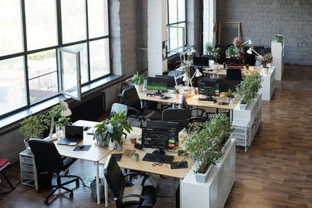 Group of desks with computer monitors standing along large windows in office or classroomの写真素材