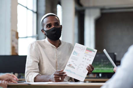 Young Muslim businessman in protective mask looking at colleague during discussionの写真素材