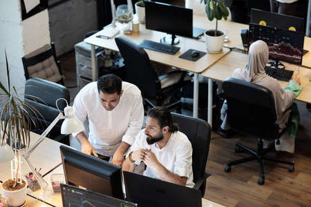 Two businessmen discussing data on computer screen while working in officeの写真素材
