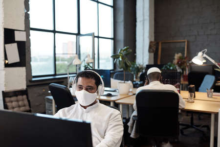 Young contemporary office manager in protective mask working in the net in front of computerの写真素材