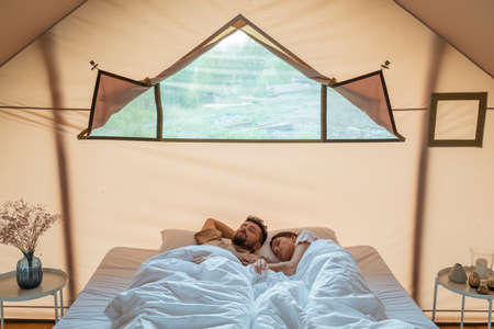 Young husband and wife sleeping on large double bed inside glamping tentの写真素材
