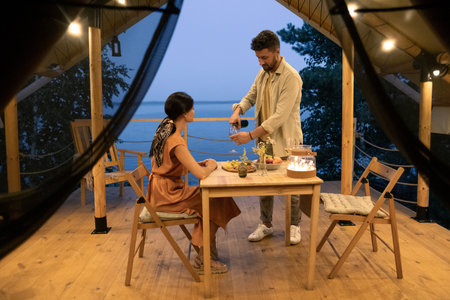 Young couple enjoying summer evening by served table on terrace of glamping house