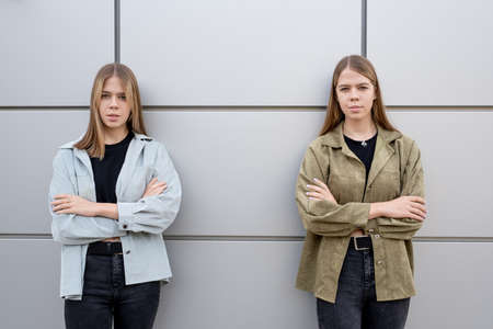 Two cute blond teenage girls in black jeans and jackets crossing arms by chestの写真素材