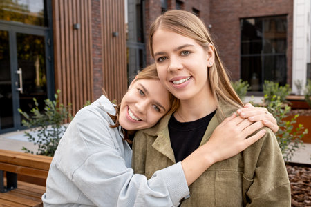 Affectionate twin girls in t-shirts and jackets looking at camera while enjoying outdoor restの写真素材