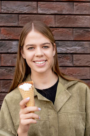 Cute blond girl in jacket holding icecream while standing against building outdoors