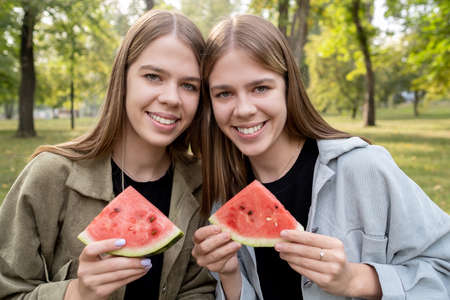 Two cute girls with slices of watermelon resting in park on summer dayの写真素材