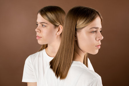Two cute blond teenage girls in white t-shirts standing against brown backgroundの写真素材