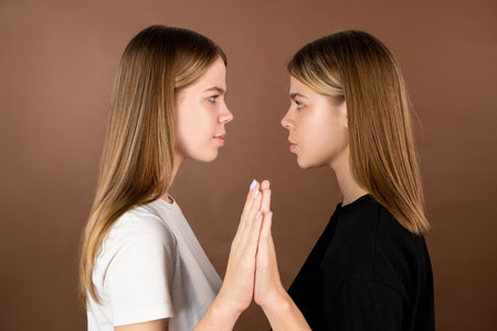 Side view of twin teenage girls touching by hands and looking at one anotherの写真素材