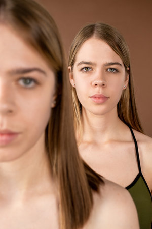 One of blond pretty twin girls standing behind her sister in front of cameraの写真素材