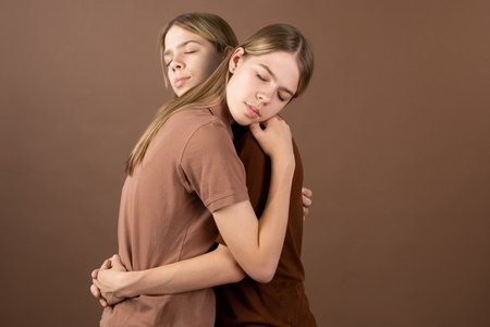 Affectionate twin girls in shirts standing in embrace in front of cameraの写真素材