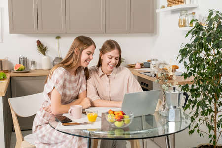 Two contemporary teenage girls video calling in front of laptop in kitchen environmentの写真素材