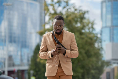 Young businessman with earphones looking through playlist in smartphone