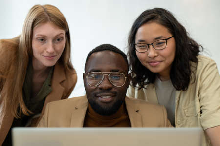 Three happy young employees looking at screen of laptop in front of cameraの写真素材