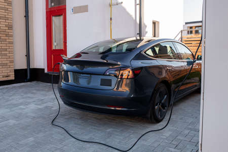 New black electric car is being charged at station in urban environment