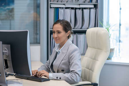 Contemporary businesswoman working in front of computer by her workplace