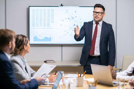 Serious business coach pointing at one of employees while answering his question during presentationの写真素材