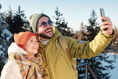 Happy young Caucasian couple making selfie in the forest while enjoying chill on winter dayの写真素材