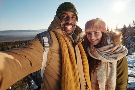 Happy multiracial couple making selfie while standing against natural environmentの写真素材