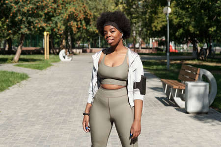 Happy active female in sportswear looking at you while standing on road in parkの写真素材