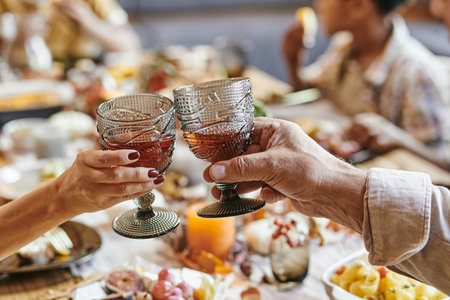Close-up of senior couple toasting with glasses with red wine while sitting at dining table with familyの写真素材