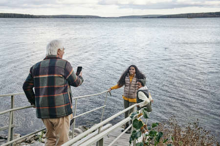 Grandchildren standing on the bridge and posing to their grandfather while he photographing them against the lake outdoorsの写真素材
