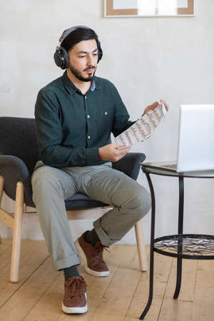 Young music teacher in headphones showing notes to student on laptop screen during online lessonの写真素材