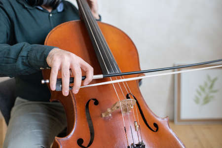Hand of young cello player gliding fiddlestick across strings while performing piece of music in front of cameraの写真素材