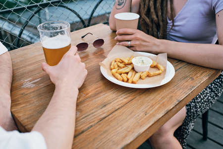 Young restful couple having drinks and french fries while sitting by table in cafe