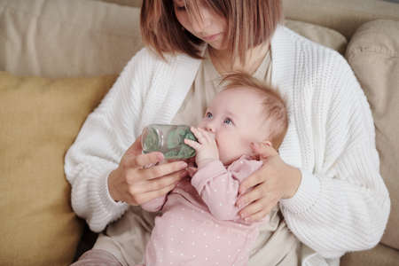 Cute little baby girl on mother hands drinking water from bottle in front of cameraの写真素材