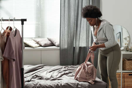 Young sportswoman in activewear putting handbag on bed while getting ready for outdoor trainingの写真素材