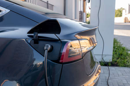 Side view of back part of black electric car with plugged charging cable at fueling stationの写真素材