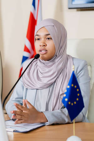 Confident muslim representative of European Union in hijab touching tips of fingers while speaking...