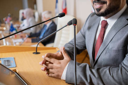 Close-up of smiling male politician with clasped hands standing at rostrum and answering questions...