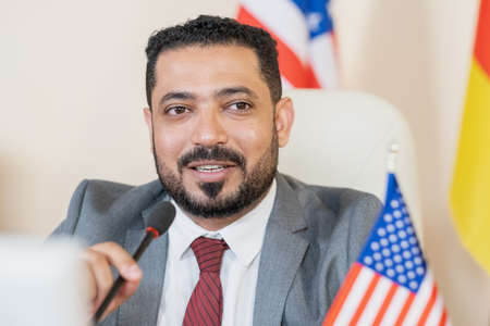 Confident American Arabian politician with beard speaking into microphone while talking to...