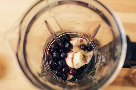 Fresh peeled and chopped banana and blueberries prepared for cooking homemade smoothie or yoghurt in electric blenderの写真素材