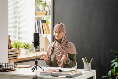 Young confident woman in hijab looking at smartphone camera during onlnie training or educational livestreamの写真素材