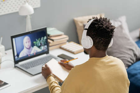 Young African male student in headphones looking at teacher on laptop screen explaining new subject during online lessonの写真素材