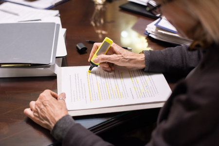 Hands of contemporary female lawyer with yellow highlighter underlining the main terms of contract...