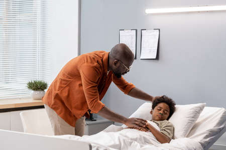 African father caring about his little son while he lying in hospital bed during his diseaseの写真素材