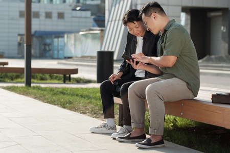 Young businessman in casualwear showing his female colleague online video in his smartphone while...