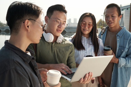Four young Chinese employees gathered for working meeting standing by riverside and watching...