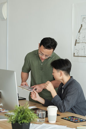 Two young designers of Asian ethnicity discussing color samples for new project at working meeting in officeの写真素材