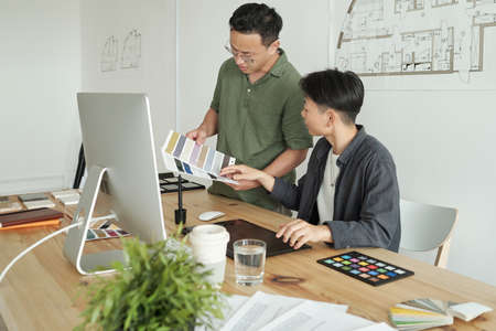 Two young contemporary architects choosing colors for interior while having meeting by workplace in...